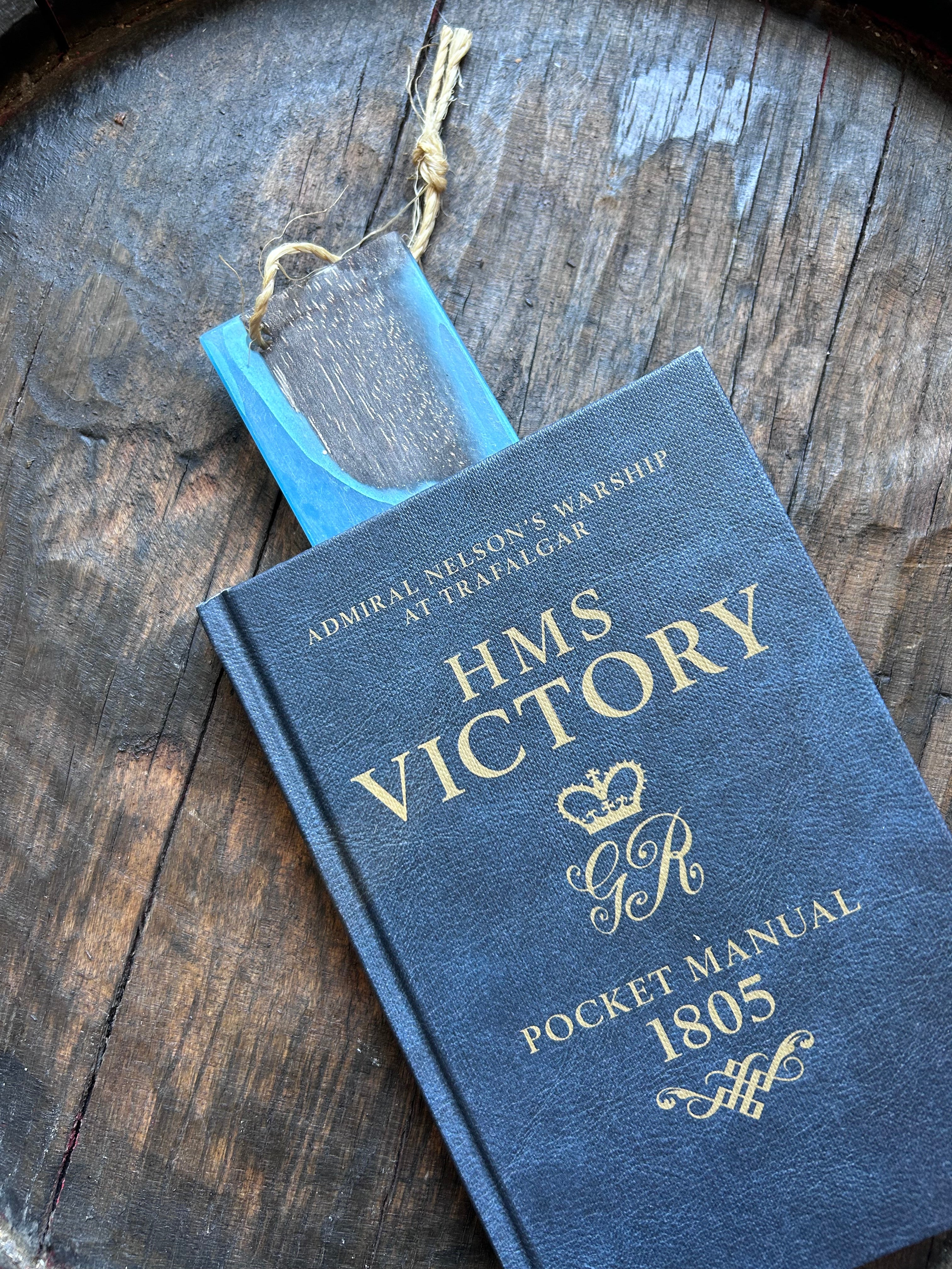 Blue book titled 'HMS Victory Pocket Manual' on a wooden surface