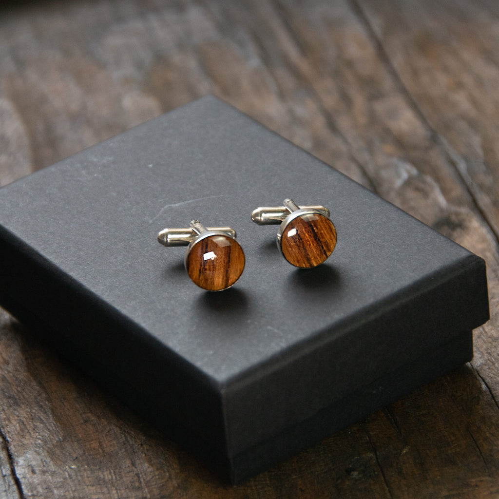 A pair of round wooden cufflinks sitting on a presentation box