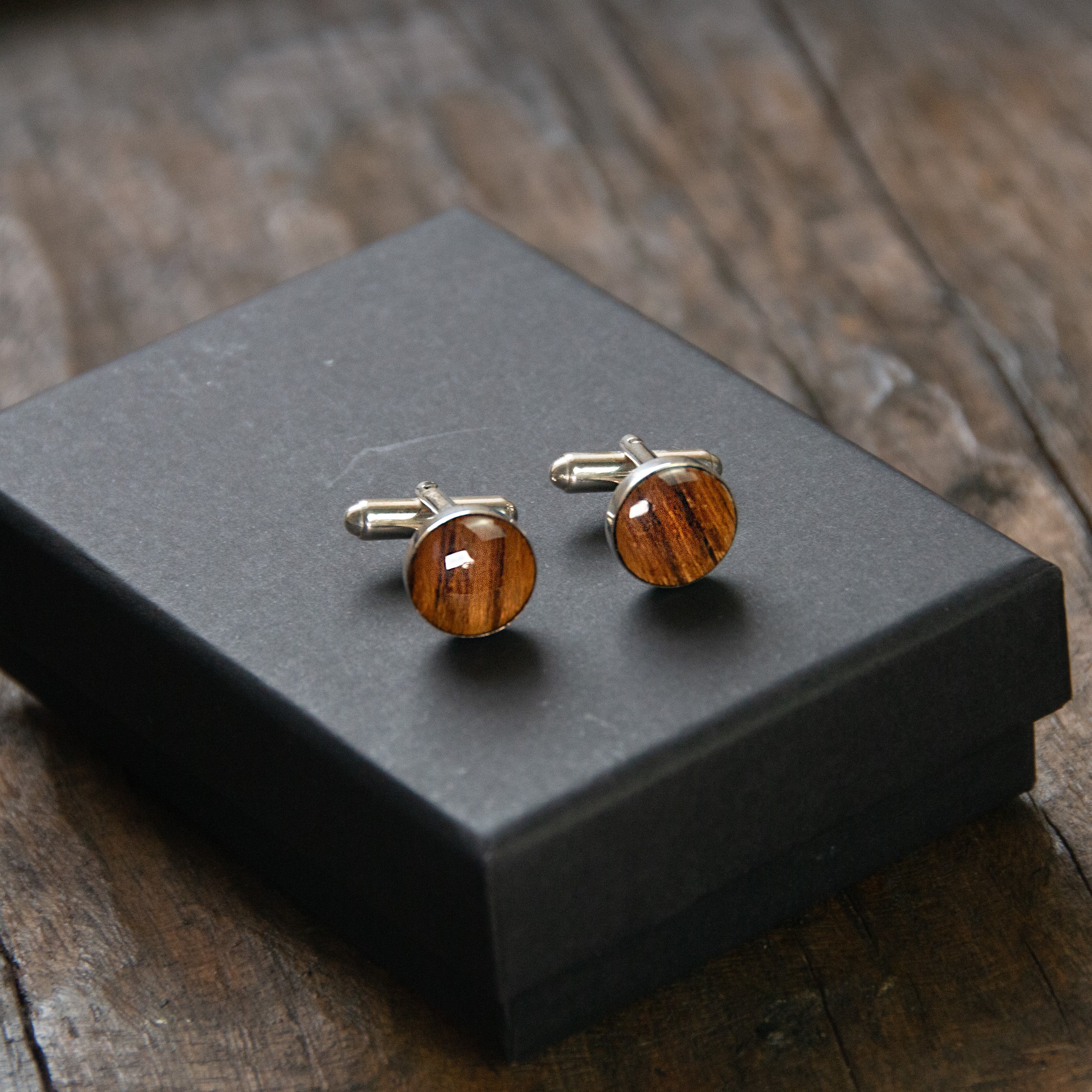 A pair of round wooden cufflinks sitting on a presentation box