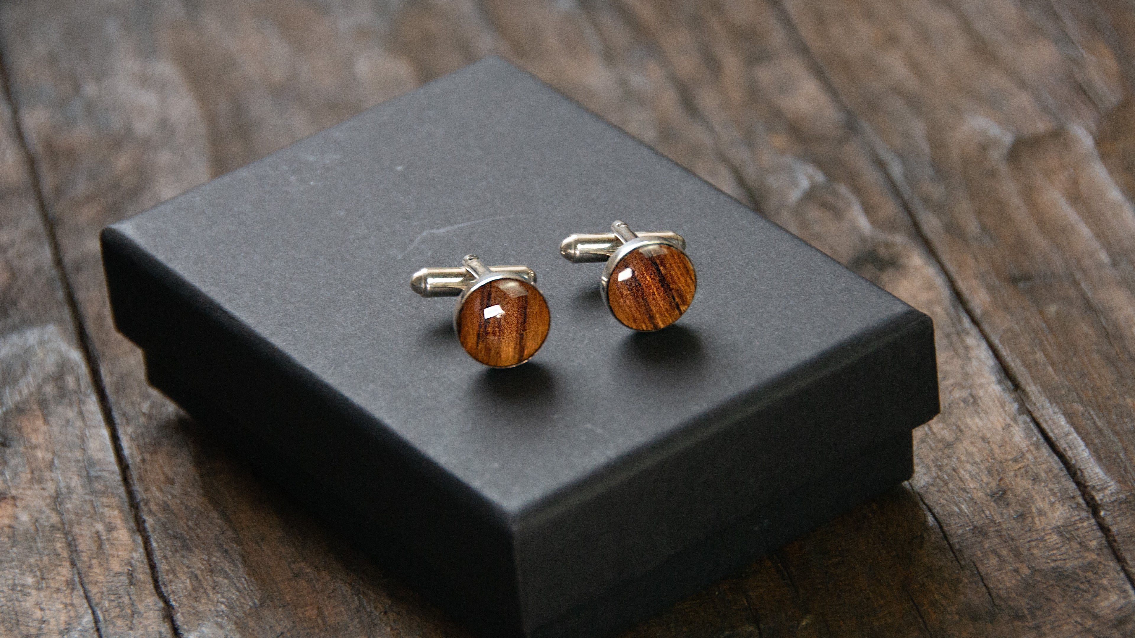 A pair of round wooden cufflinks sitting on a presentation box