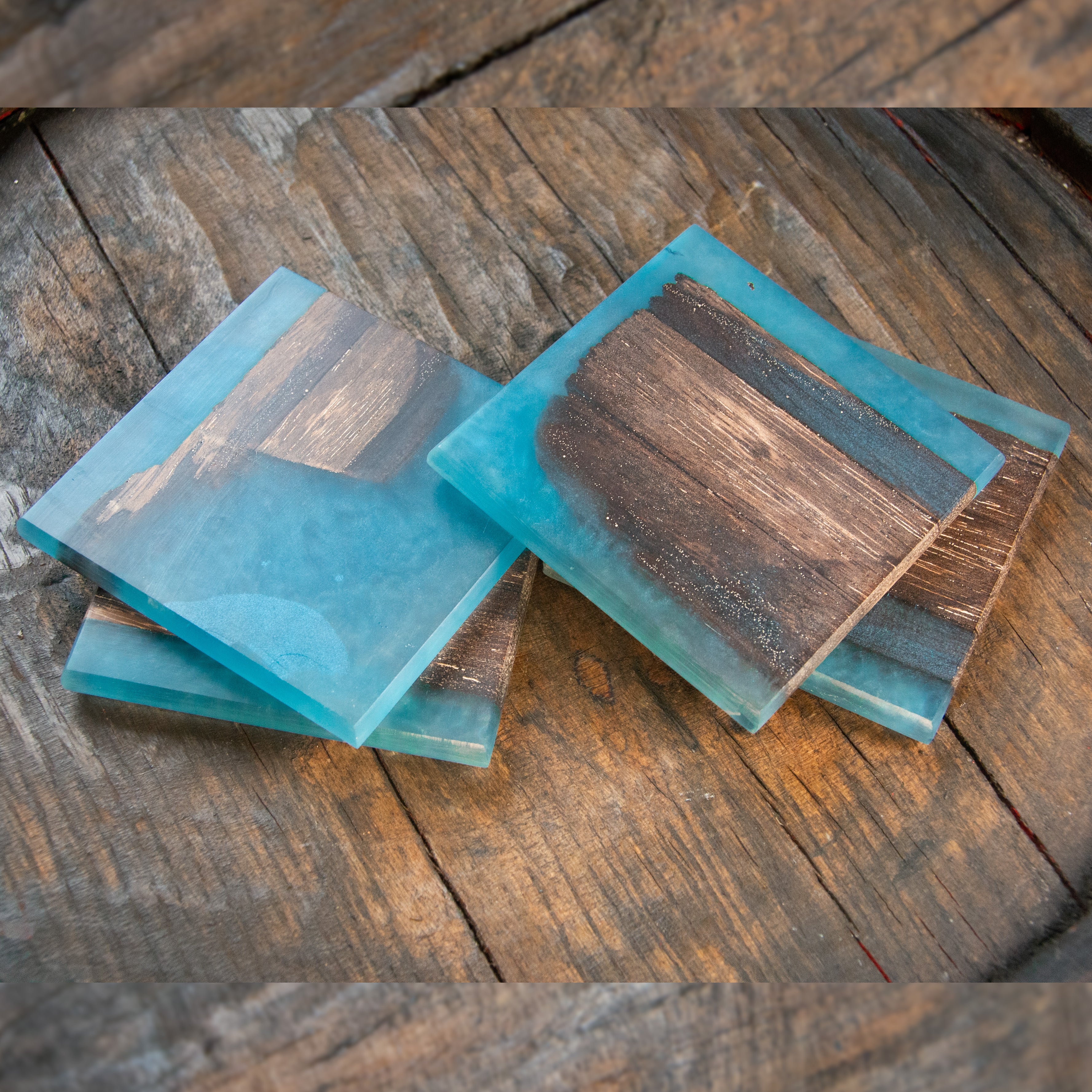 Four turquoise resin coasters, containing pieces of oak timber, on a wooden surface