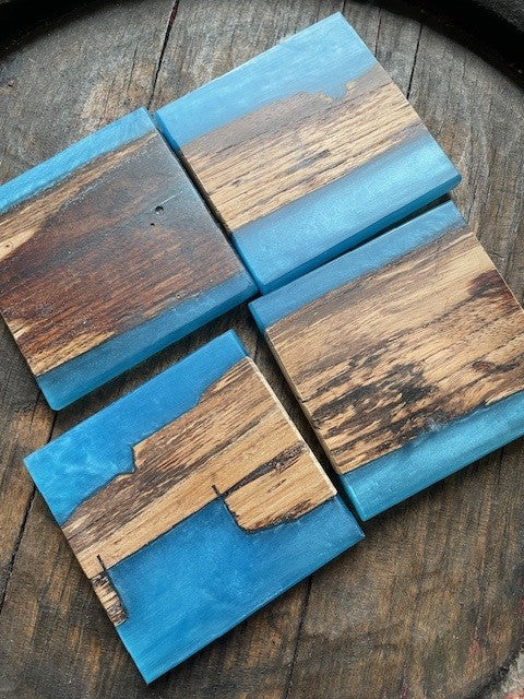 Four wooden coasters with blue resin on a wooden surface
