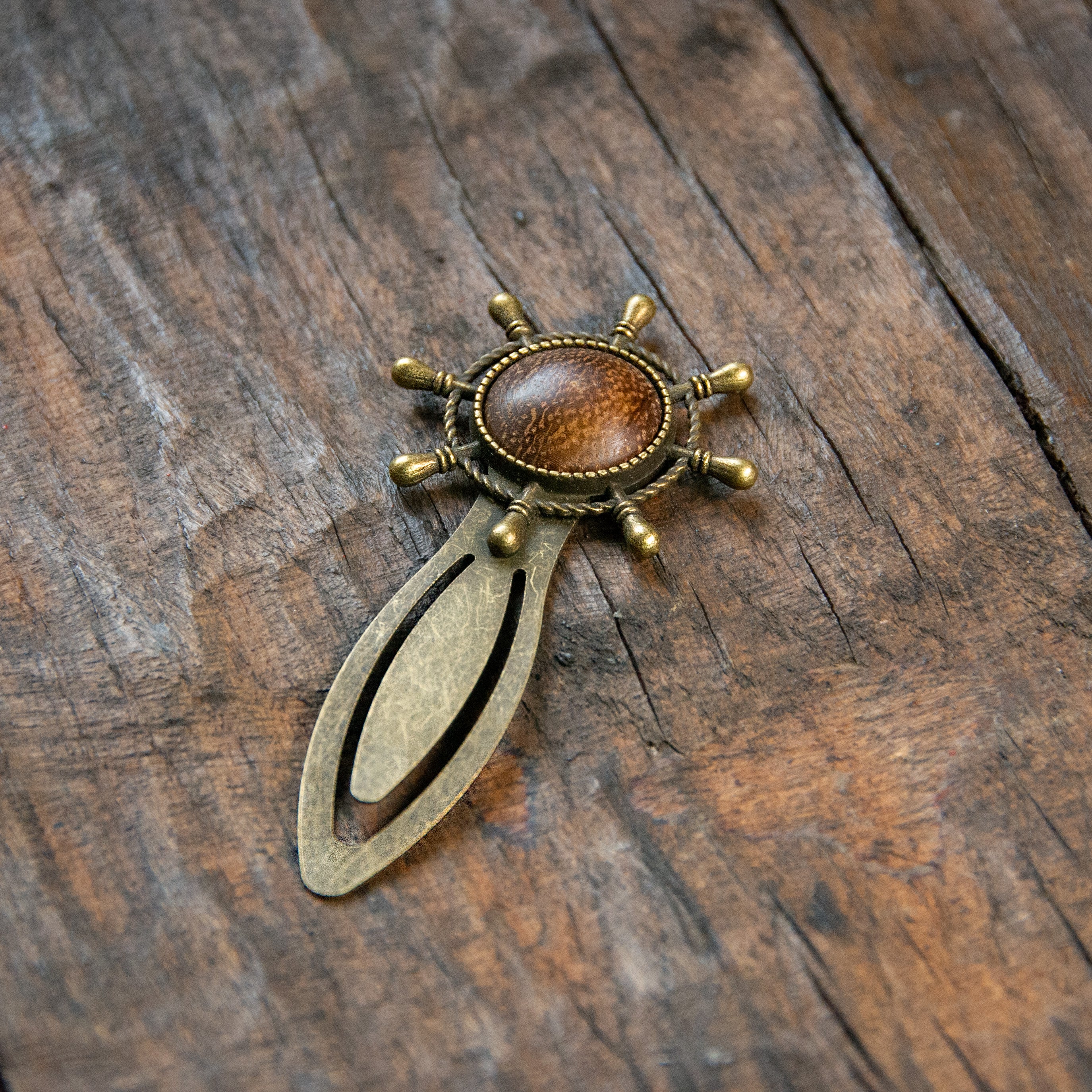 A brass clip-style bookmark, with a whips wheel with an oak button embedded i the middle.