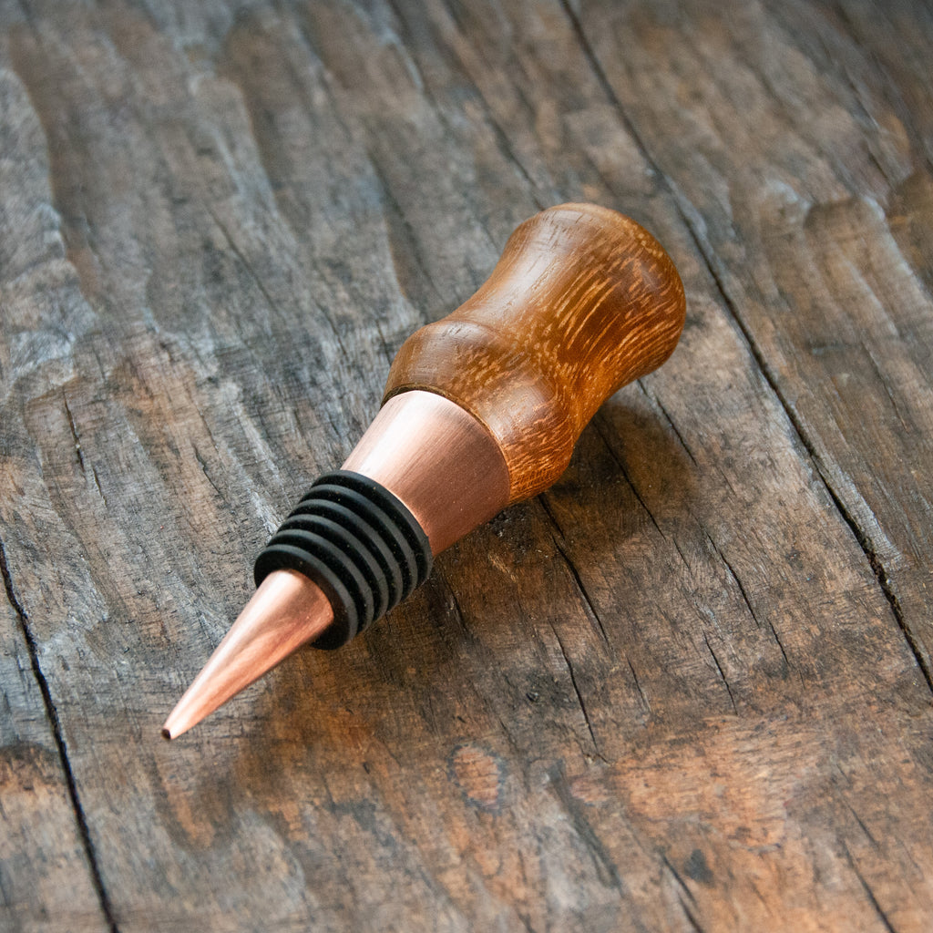 a modern bottle stopper with a copper finnish, with a handle made of oak.