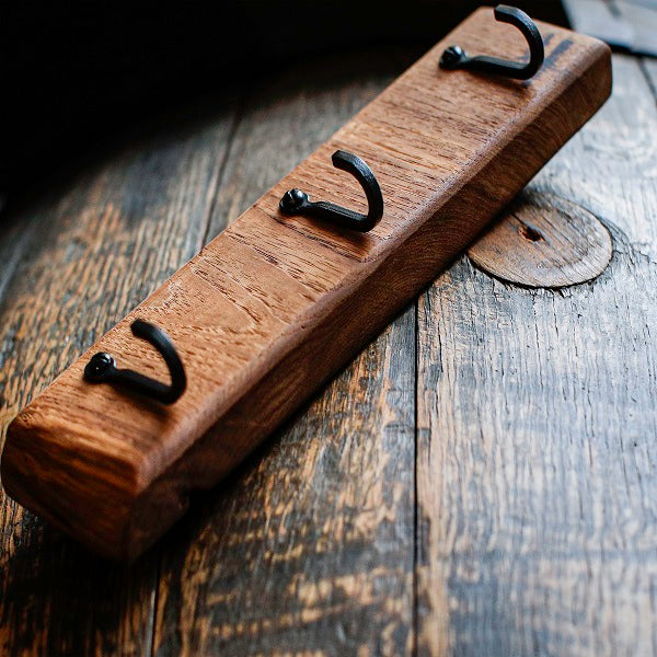 Wooden hook rack with three black hooks on a rustic wooden surface