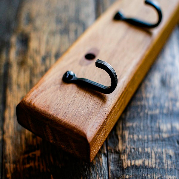Wooden plaque with black metal hooks on a rustic wooden surface