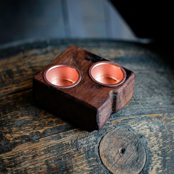 Wooden candle holder with two copper cups on a rustic wooden surface