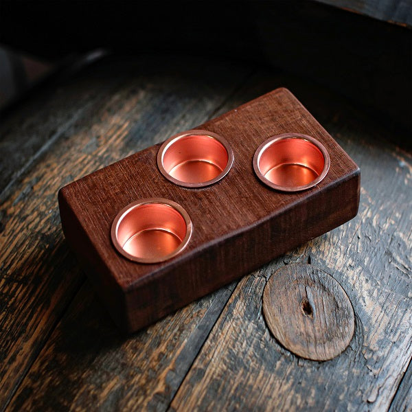 Wooden holder with three copper cups on a rustic wooden surface
