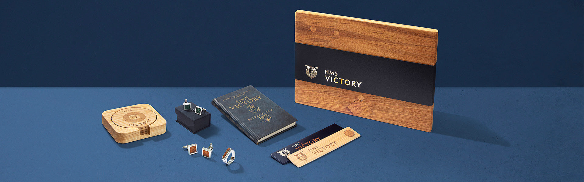 Collection of wooden and leather items including a wallet, notebook, and card holder on a blue background.