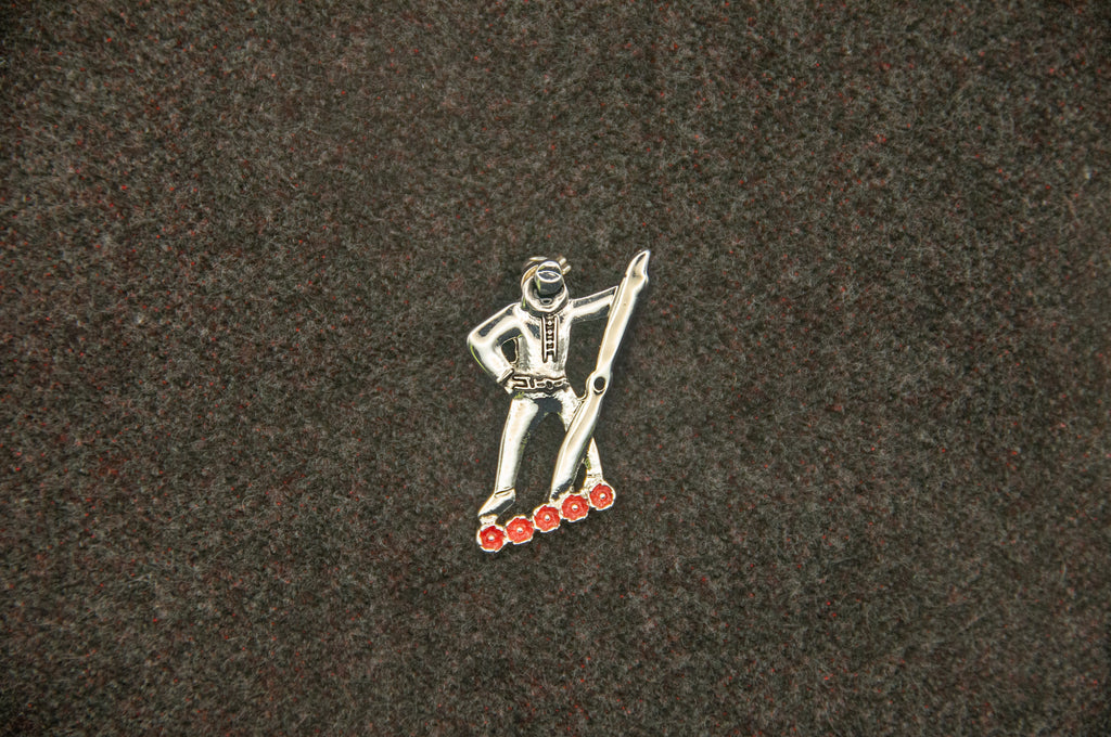 Metallic pin of a figure holding a propellor, standing above five red poppies.