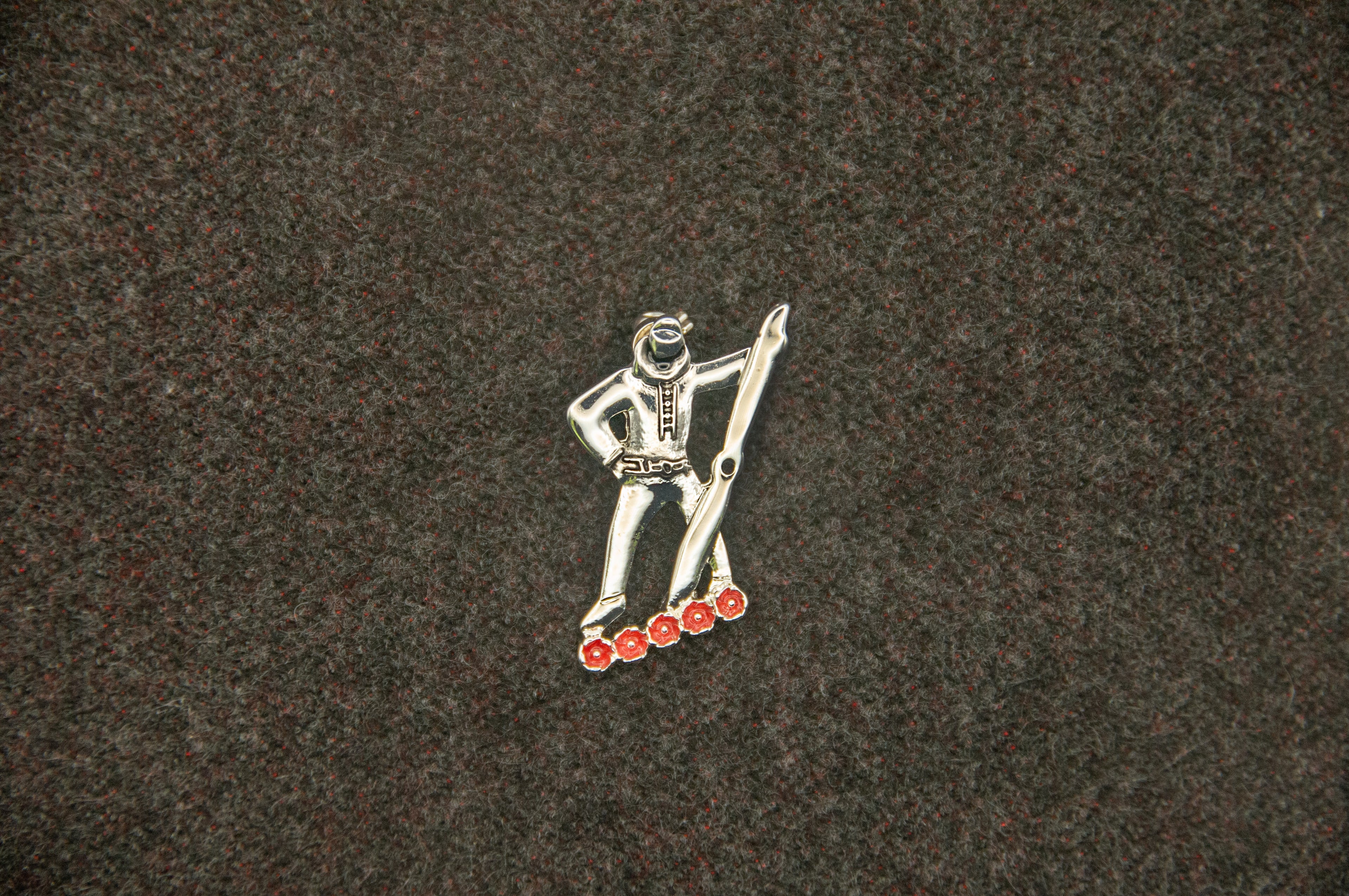 Metallic pin of a figure holding a propellor, standing above five red poppies.