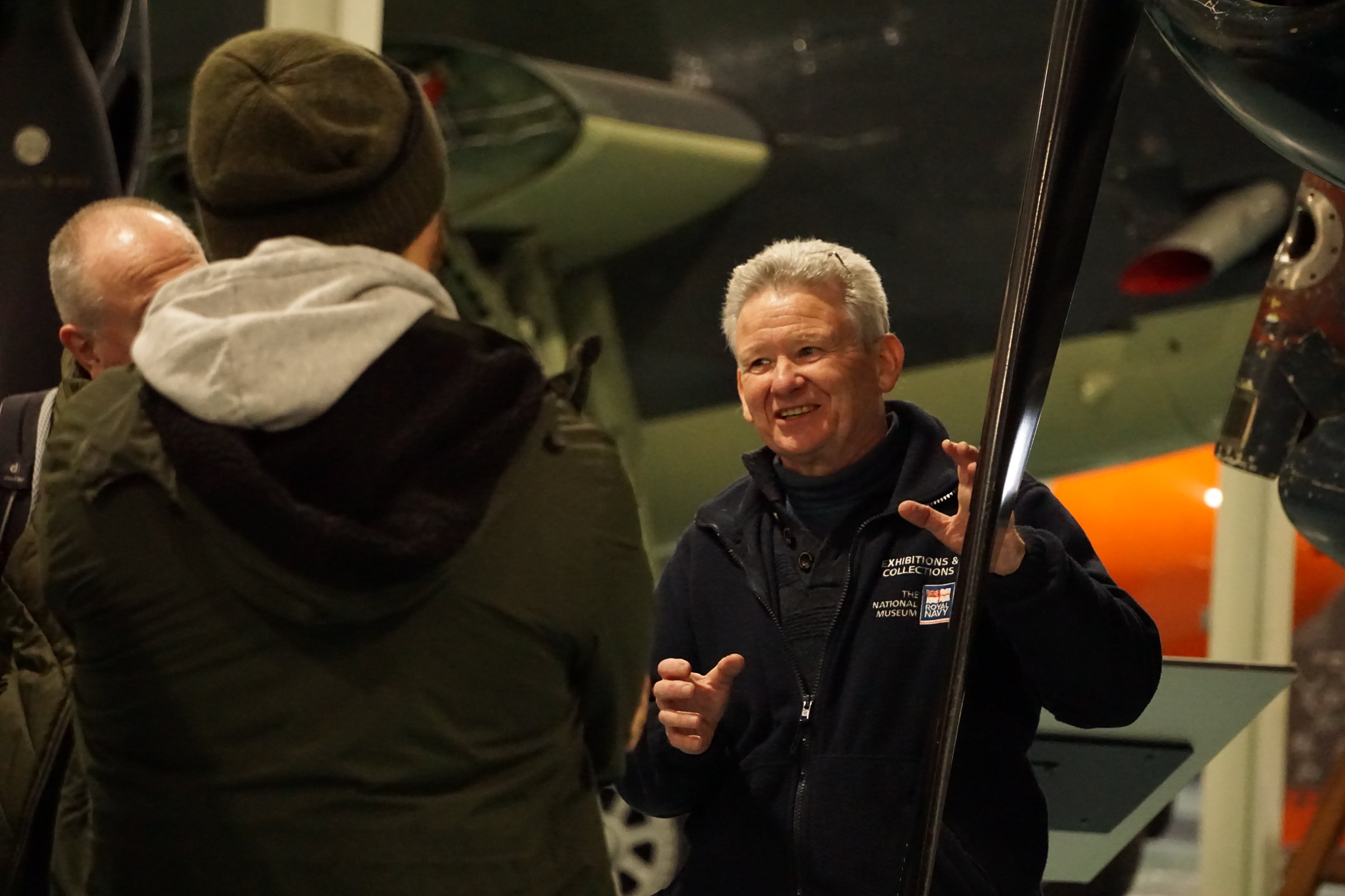 Man in a dark jacket pointing at an airplane with people around him